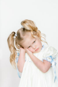 Pouting toddler girl stands in front of a white backdrop during heirloom portrait session with Morgan Leigh Photography.