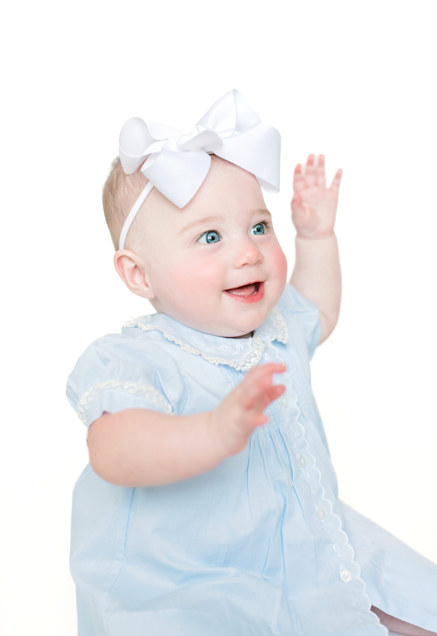 Beautiful infant girl in a blue dress laughs and waves her hands during a sitter session with Morgan Leigh Photography.