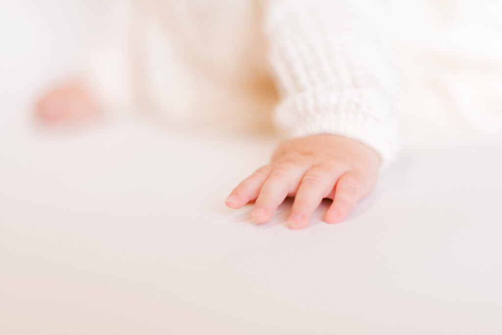Tiny hands crawl on a white backdrop during a children's portrait session.