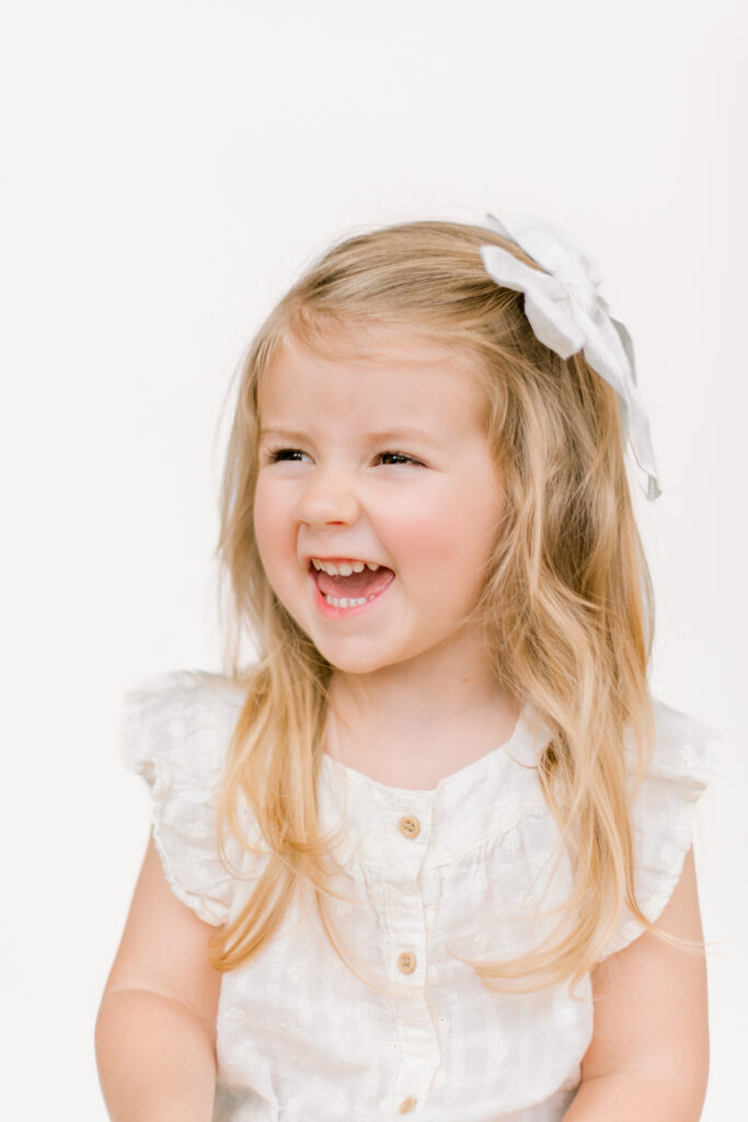 Looking off to the left, a beautiful toddler girl smiles during a session by Morgan Leigh Photography.