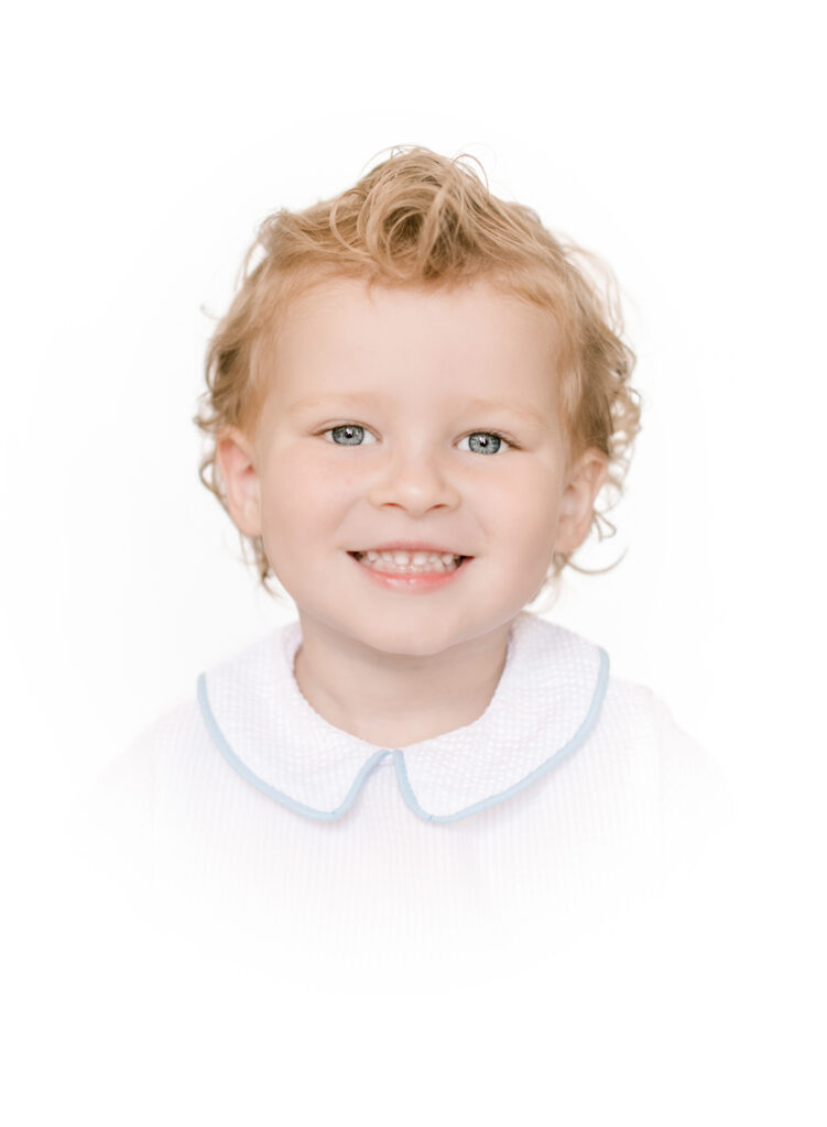 Sweet young man with curly blonde hair wears a blue trimmed collar white shirt for studio portraits.