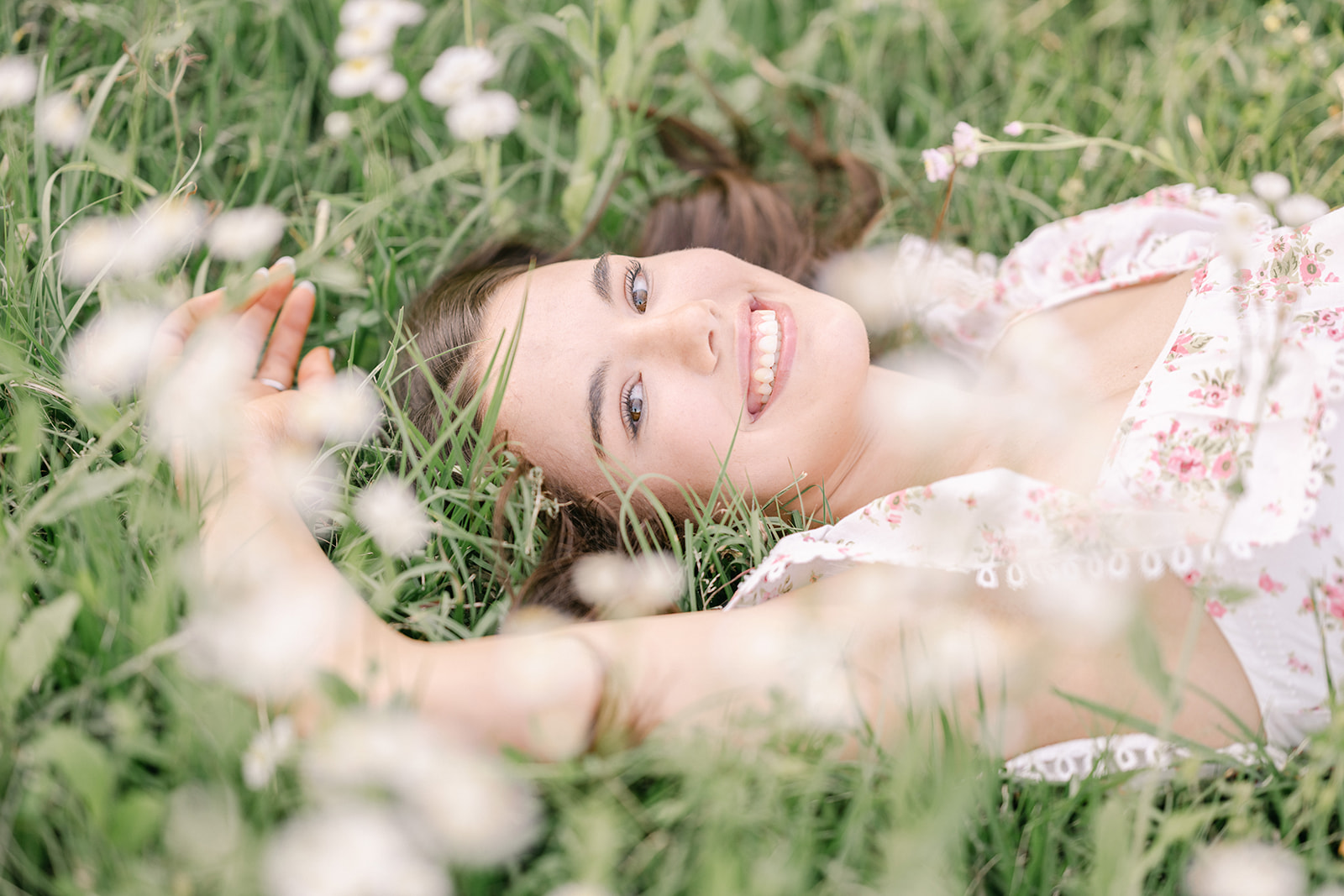 Beautiful senior girl in a floral dress lays in a field of flowers for a senior photo session by Morgan Leigh Photography in Baton Rouge
