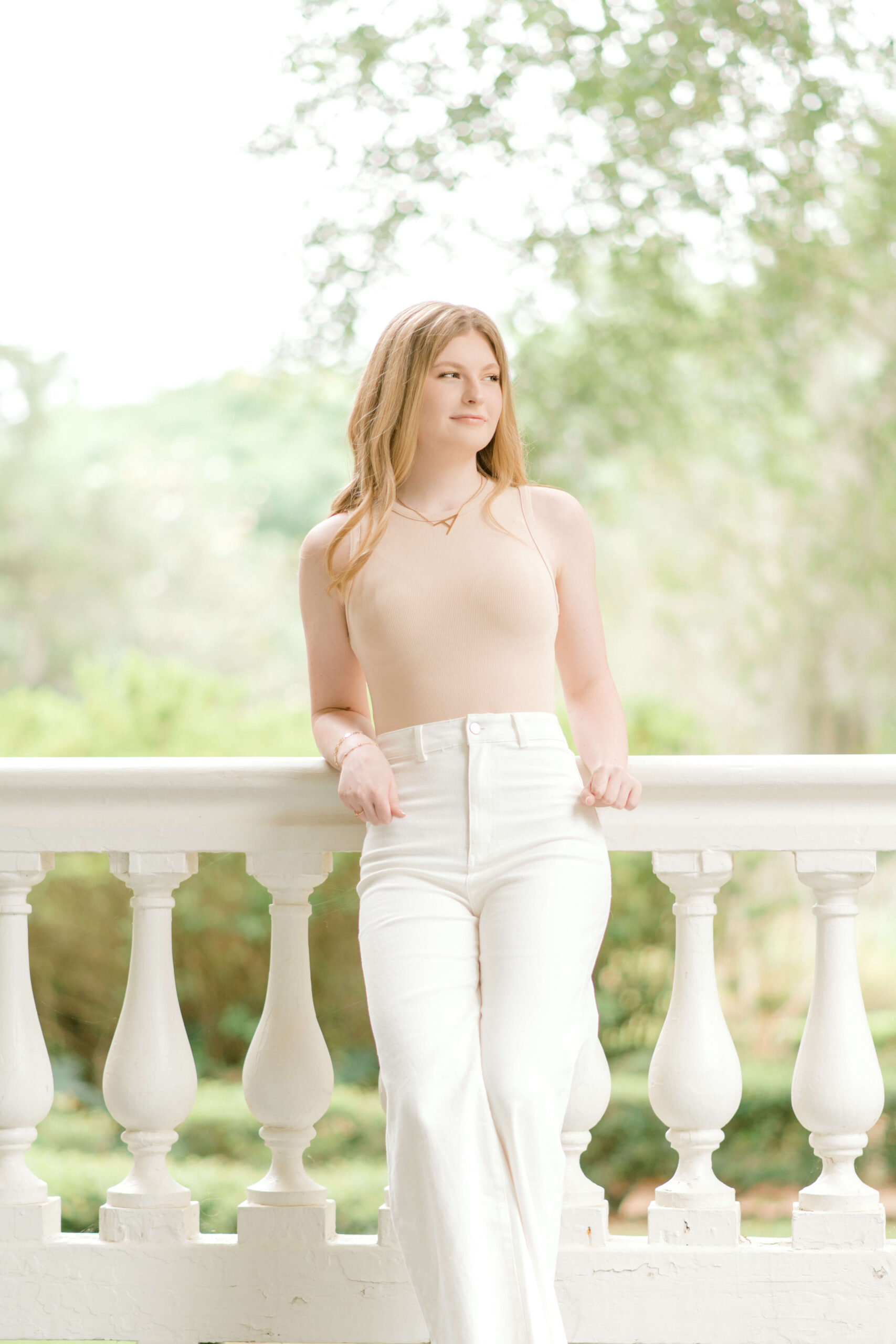 Senior girl in white jeans and a neutral top poses on the porch of Rosedown Plantation.