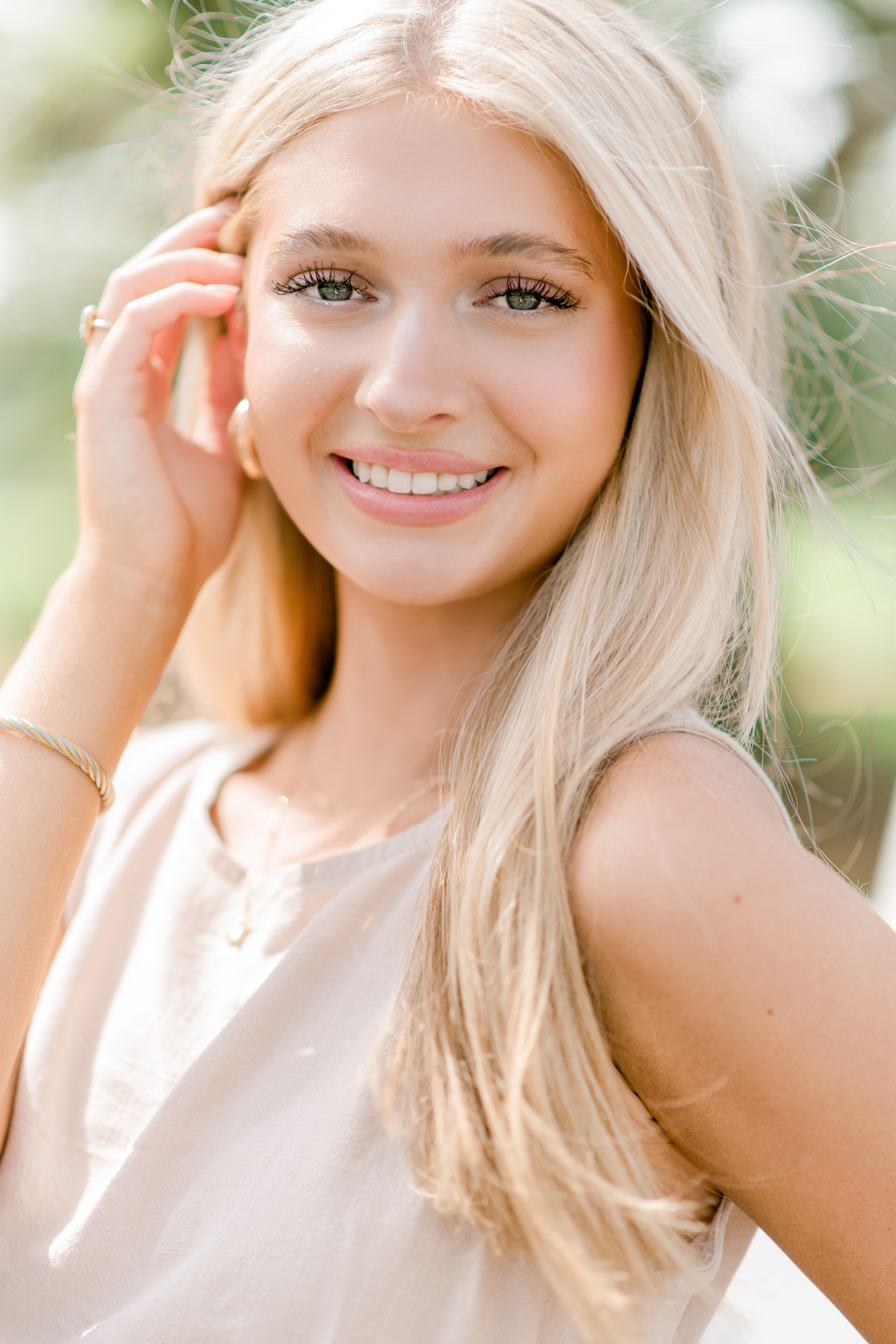 A gorgeous blonde senior girl pulls her hair back behind her right ear on a sunny day during senior portraits in Baton Rouge.