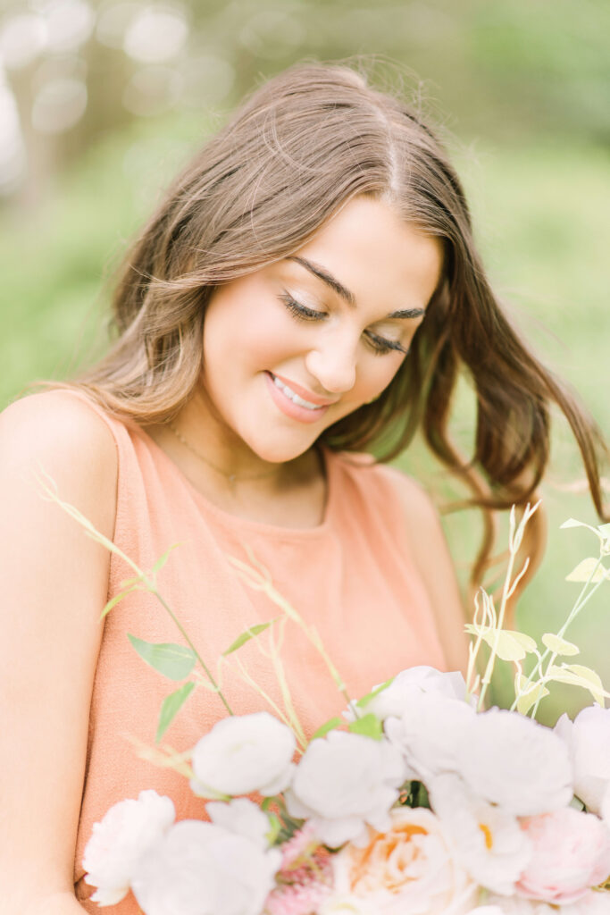 Baton Rouge senior girl smiles down at a beautiful bouquet of light flowers with her hair blowing in the breeze.