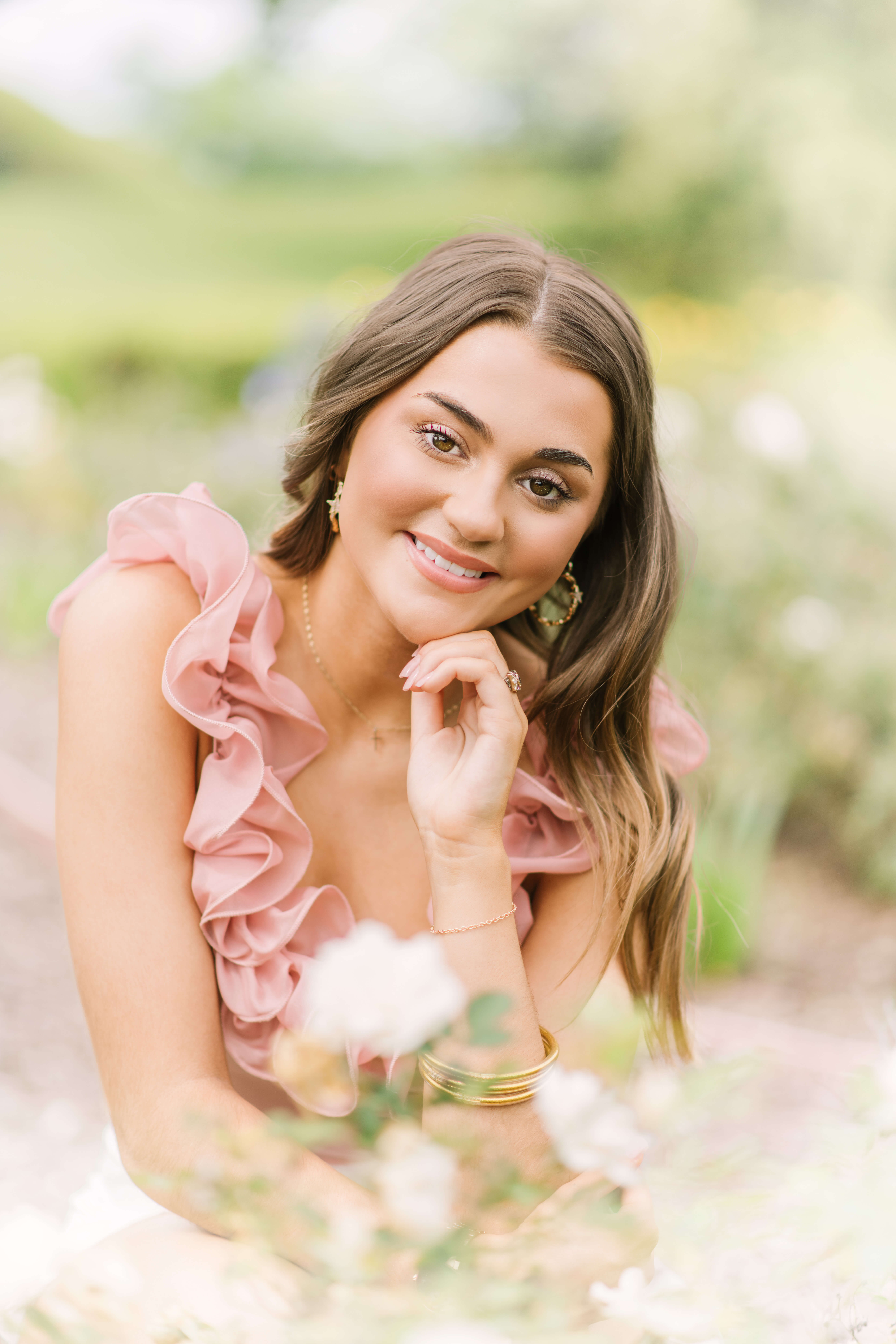 Brunette girl sits behind a white rose bush during senior portraits with Morgan Leigh Photography.