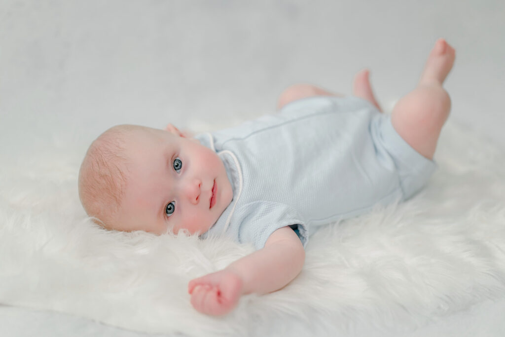Beautiful little baby boy wearing blue romper lays on painted backdrop.