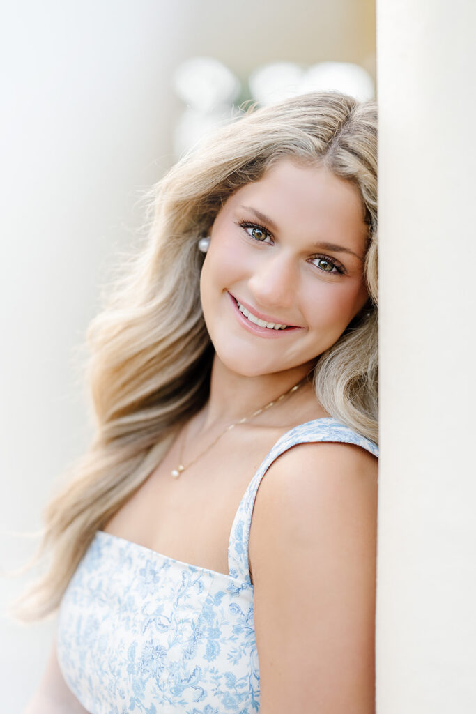 Senior in blue dress from Baton Rouge clothing boutique leans on column during session with Morgan Leigh Photography.