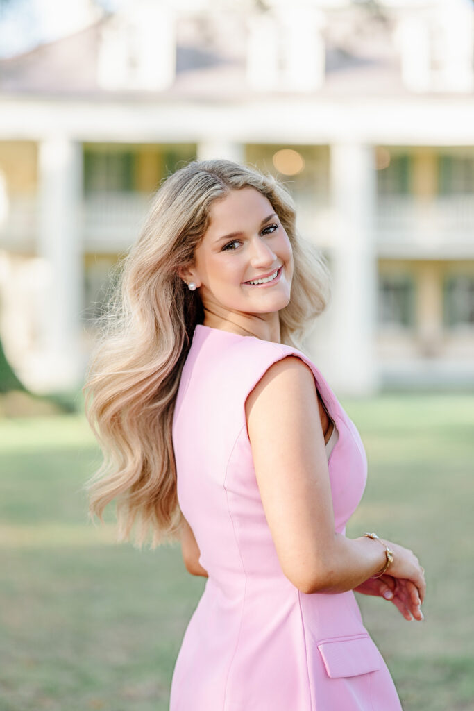 Senior in pink dress poses outside Houma's House.