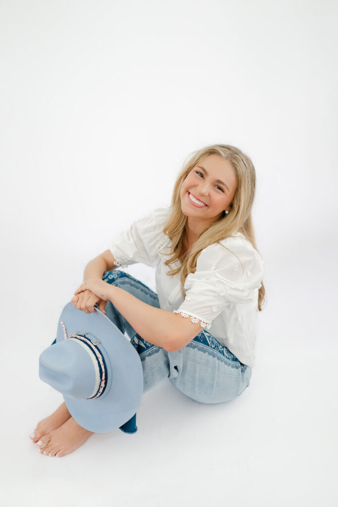 Senior girl sits in front of a white backdrop for senior portraits.