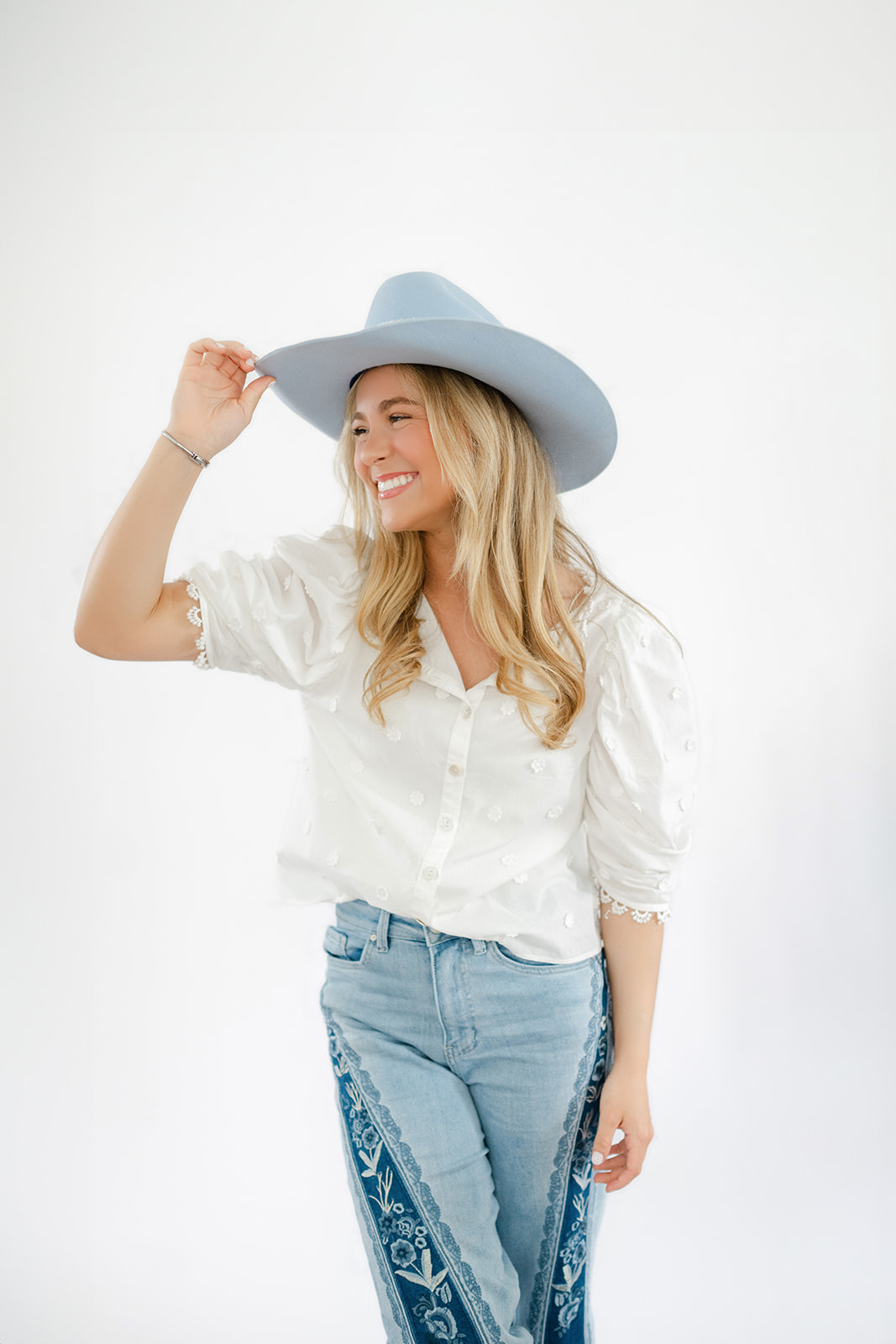 Senior grasps tip of blue cowboy hat for session with Morgan Leigh Photography.