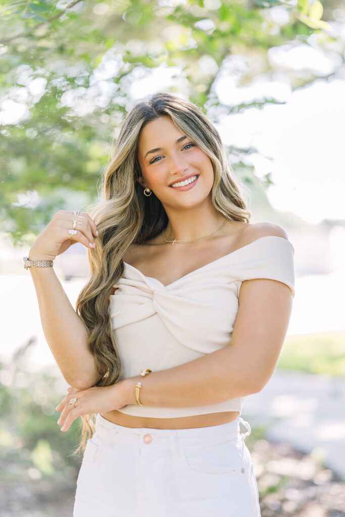 Senior girl in white top and jeans twirls her hair during Baton Rouge session.