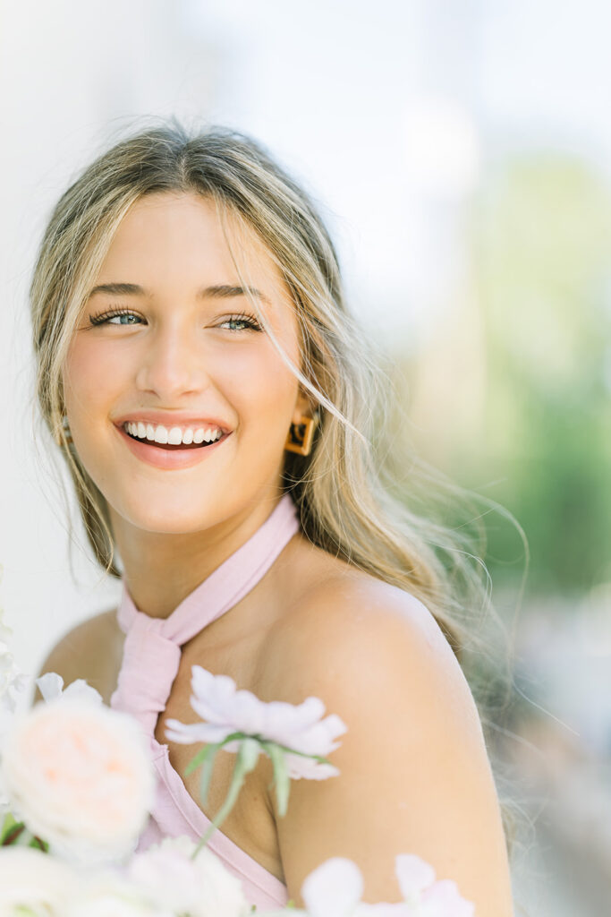 A Baton Rouge senior graduate holds a bouquet and looks off laughing.