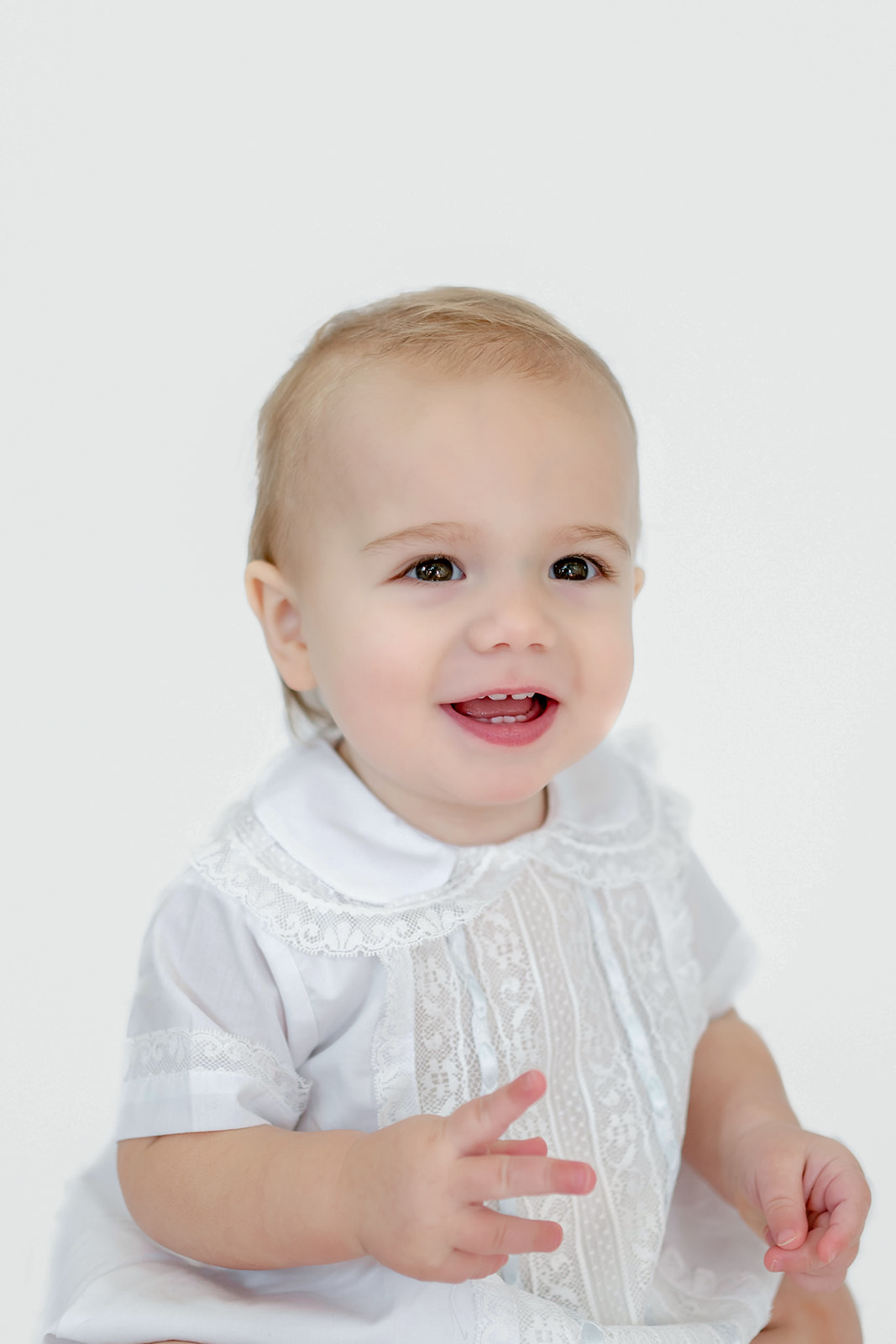 Toddler sits in front a white backdrop and smiles for heirloom photos with Morgan Leigh Photography wearing clothing from Olly-Olly Children's Store Baton Rouge.
