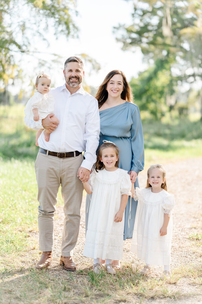 Family of parents and three daughters in light clothing take fall pictures in a field in Baton Rouge with Morgan Leigh Photography.