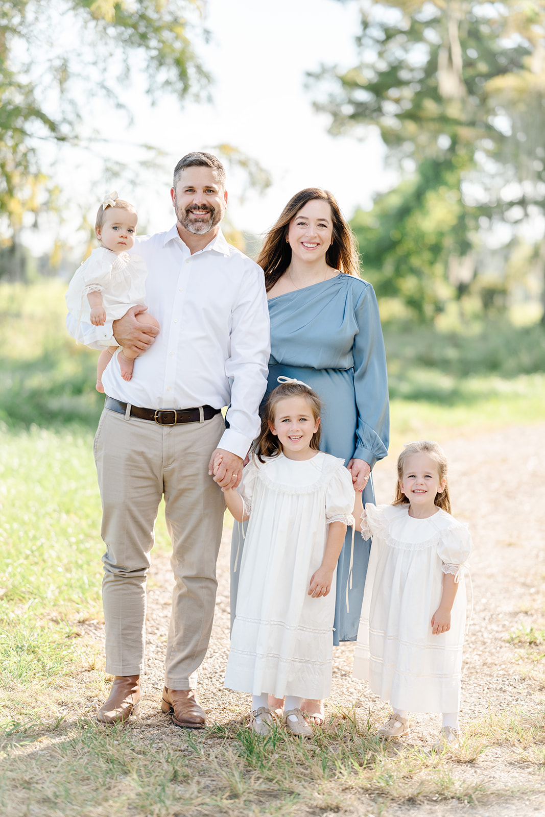 Family of parents and three daughters in light clothing take fall pictures in a field in Baton Rouge with Morgan Leigh Photography.