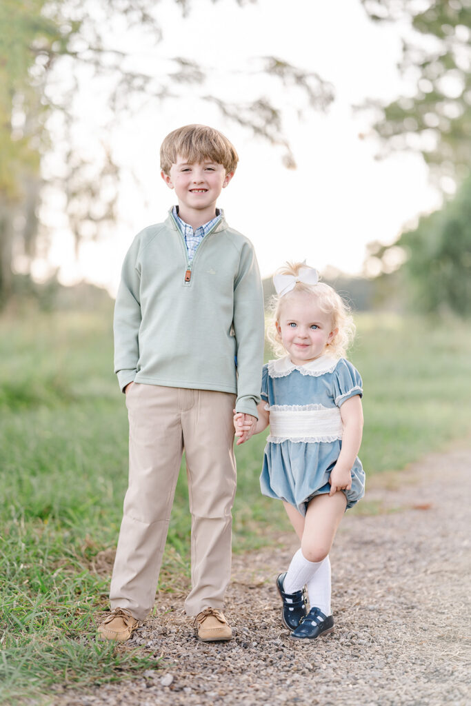Brother in green quarter zip and younger sister in light blue velvet bubble hold hands and pose for family photos with Morgan Leigh Photography in Baton Rouge, LA.