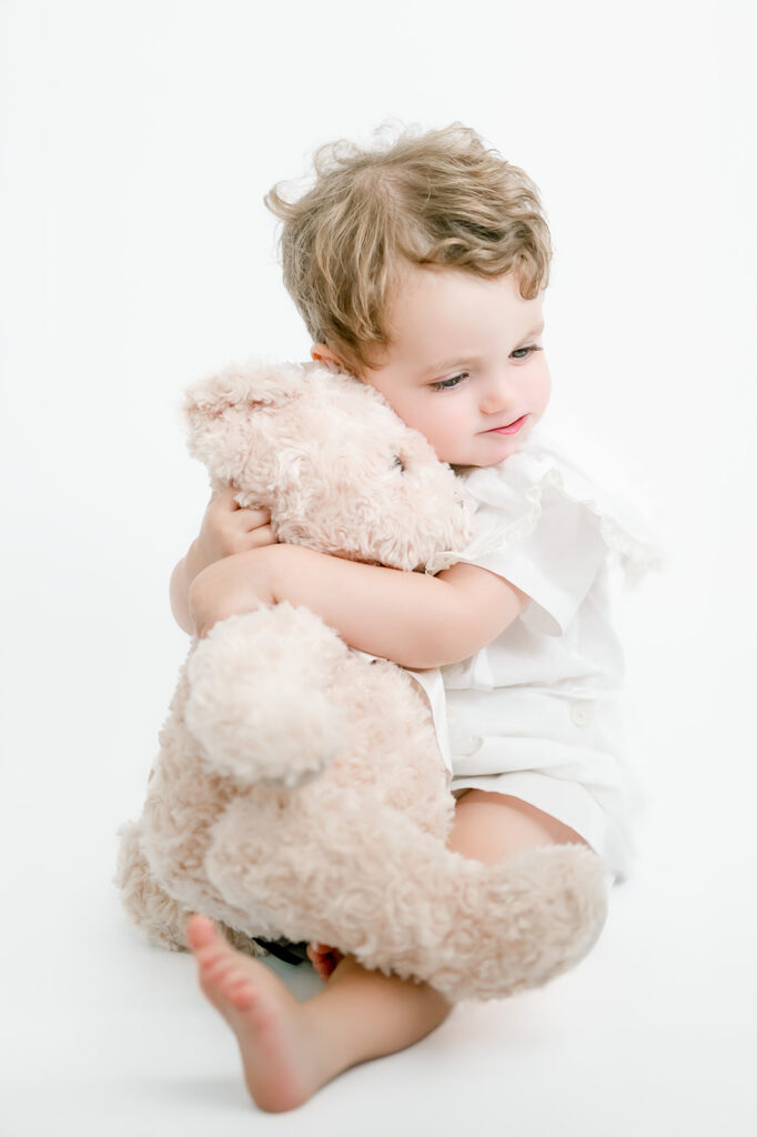 Young boy in all white hugs stuffed bear.