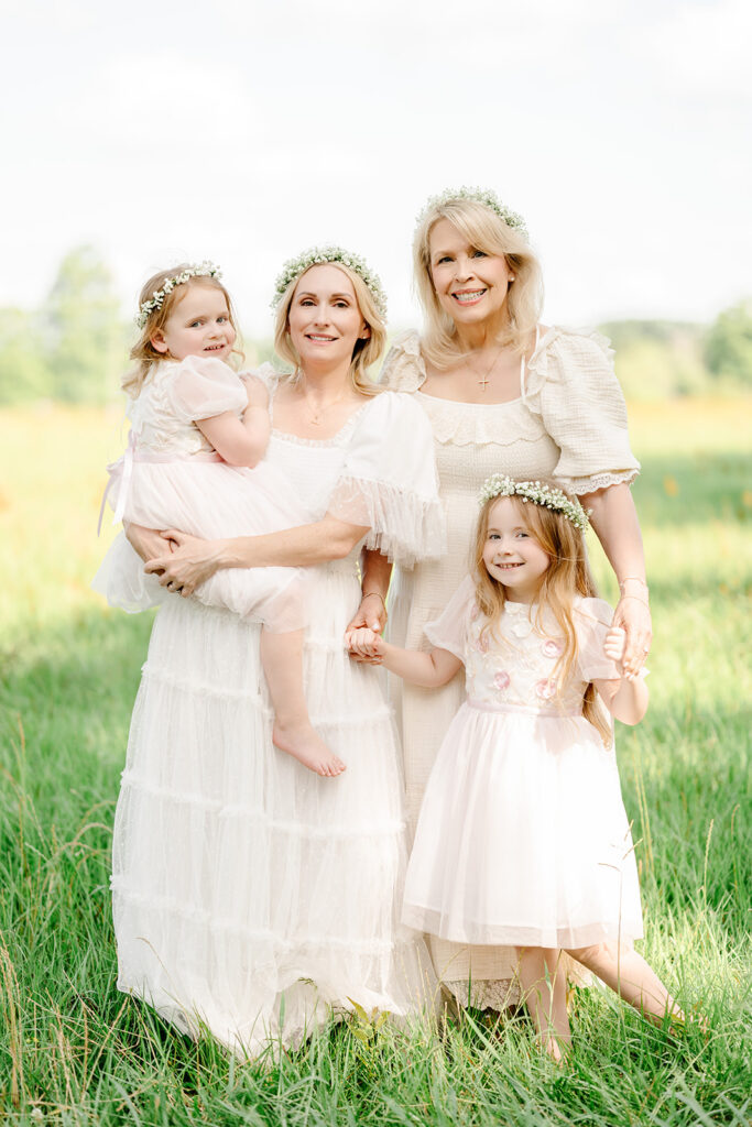 Mother, grandmother, and granddaughters in matching dresses smile in a field.